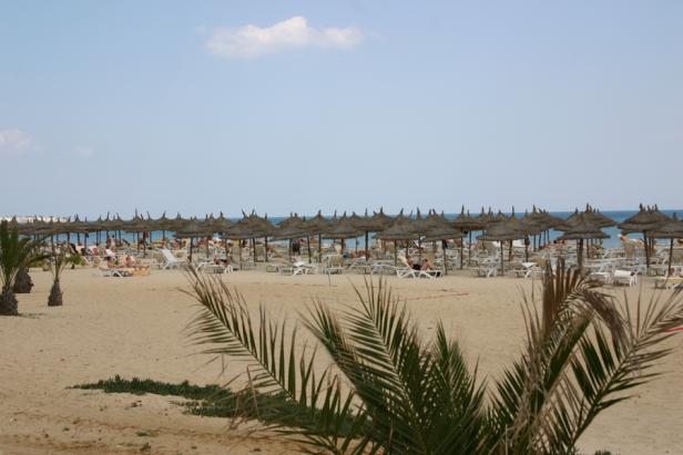 Ein Strand mit vielen Sonnenschirmen und Liegestühlen unter blauem Himmel.