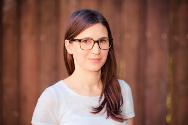 Eine junge Frau mit Brille lächelt vor einem braunen Hintergrund.