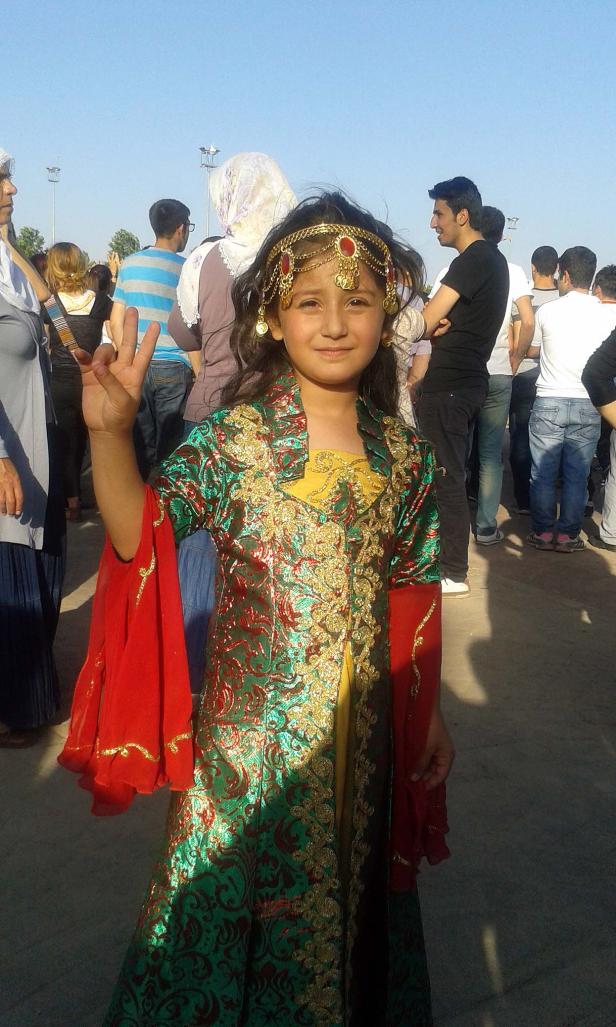 Ein junges Mädchen in traditioneller kurdischer Kleidung lächelt in die Kamera.