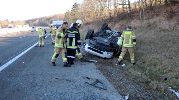 Ein auf dem Dach liegendes Auto wird von Feuerwehrleuten begutachtet.