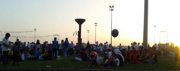 Eine Menschenmenge versammelt sich auf einer Wiese unter einem hellen Himmel.