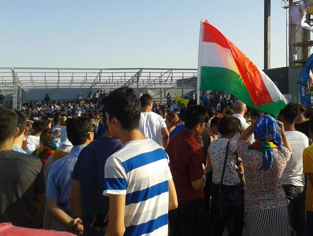 Eine Menschenmenge versammelt sich unter einer kurdischen Flagge.