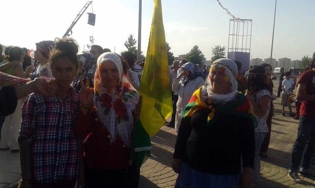 Eine Gruppe von Frauen mit Kopftüchern und einer gelb-grünen Flagge demonstriert auf einem Platz.
