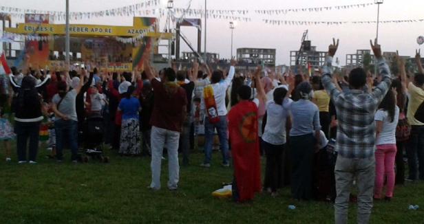 Eine Menschenmenge demonstriert mit erhobenen Händen auf einer Wiese vor einer Bühne.