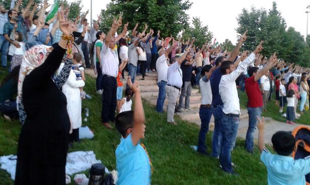 Eine große Menschenmenge, die auf einer Wiese steht und ihre Hände mit dem Victory-Zeichen in die Luft reckt.