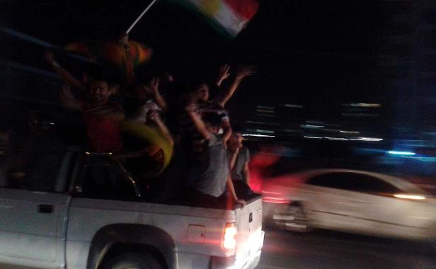 Menschen feiern auf der Ladefläche eines Pickups mit einer kurdischen Flagge.