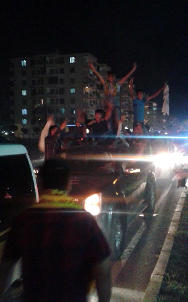 Eine Gruppe junger Leute feiert auf und um ein Auto herum in der Nacht.