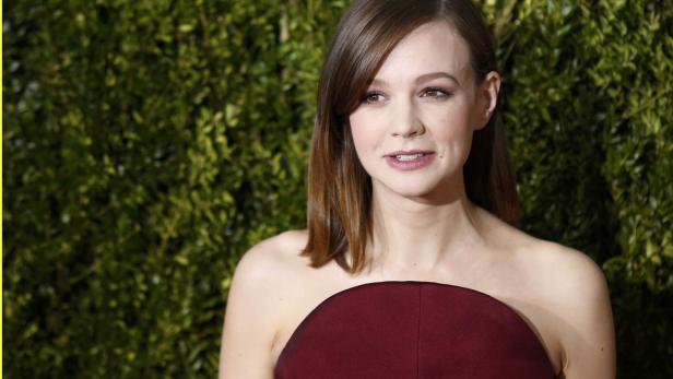 Carey Mulligan in einem trägerlosen, weinroten Kleid vor einem grünen Hintergrund.