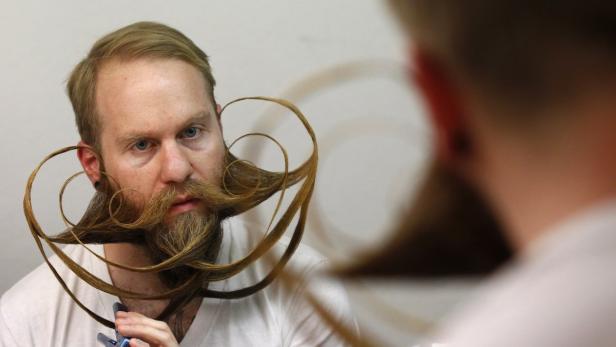 Ein Mann mit kunstvoll gezwirbeltem Bart betrachtet sich im Spiegel.