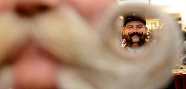 Ein Mann mit Hut und extravagant gezwirbeltem Schnurrbart blickt durch eine Röhre.