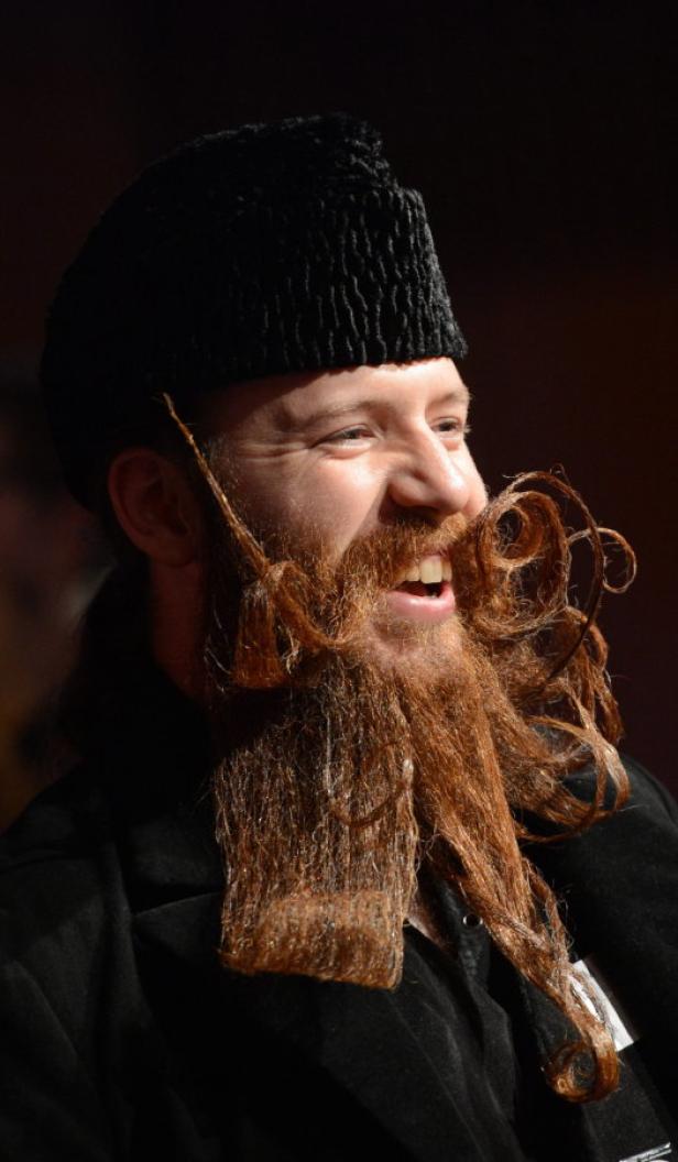 Ein Mann mit Hut und kunstvoll gestyltem, langem Bart lächelt.