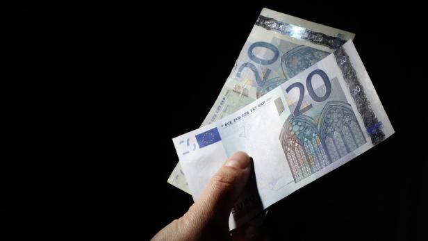 Eine Hand hält zwei 20-Euro-Scheine vor einem schwarzen Hintergrund.