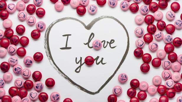 Ein gezeichnetes Herz mit der Aufschrift „I love you“, umgeben von M&Ms mit Herzen, Buchstaben und Namen.