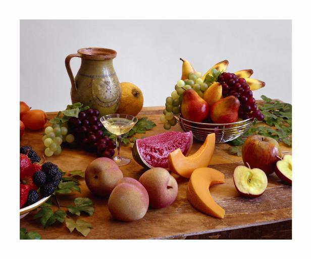 Ein Stillleben mit verschiedenen Früchten wie Melonen, Äpfeln, Birnen und Beeren auf einem Holztisch.