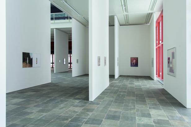 Ein Ausstellungsraum mit Kunstwerken an weißen Wänden und einem grauen Fliesenboden.