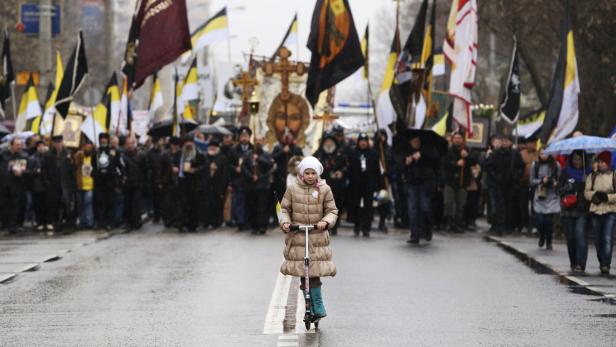Ein Mädchen fährt auf einem Roller vor einer Prozession mit religiösen Bannern.
