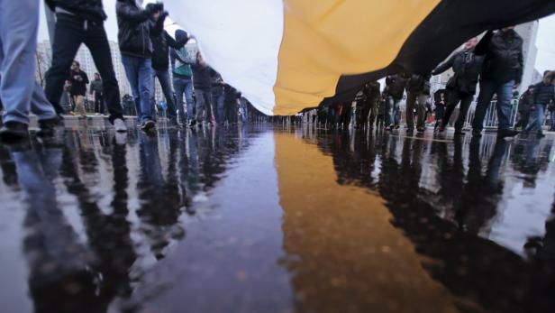 Eine Menschenmenge hält eine große Flagge auf einer nassen Straße.
