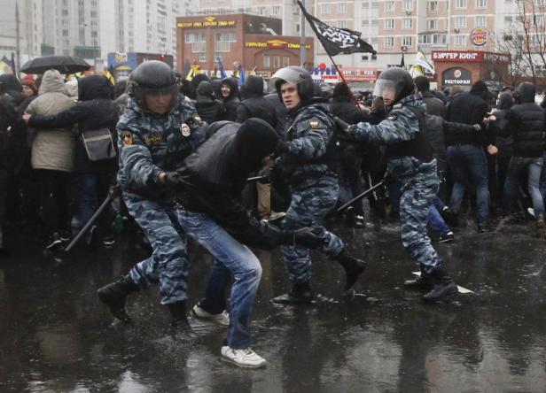 Polizisten führen eine Person bei einer Demonstration in einer regnerischen Stadt ab.
