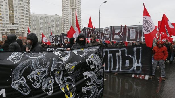 Eine Demonstration mit roten Fahnen und einem Banner mit Schlangenmotiven zieht durch die Stadt.