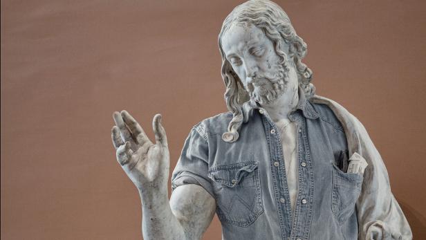 Eine Jesusstatue trägt ein Jeanshemd mit Zigarettenpackung in der Tasche.