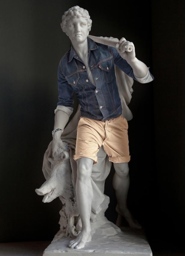 Eine antike Statue, bekleidet mit Jeansjacke und Shorts, hält einen Eber.