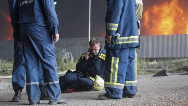 Ein verletzter Feuerwehrmann telefoniert am Brandort, umgeben von Kollegen.