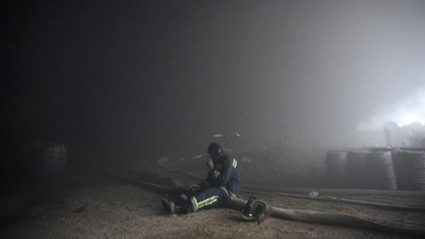 Ein Feuerwehrmann sitzt erschöpft inmitten von Rauch auf dem Boden.
