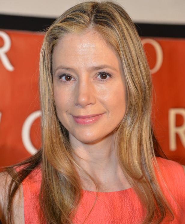 Die Schauspielerin Mira Sorvino lächelt in einem korallfarbenen Kleid.