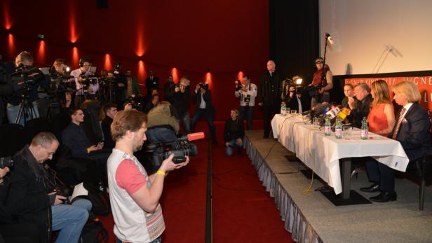 Eine Pressekonferenz mit mehreren Personen am Tisch und zahlreichen Journalisten im Hintergrund.