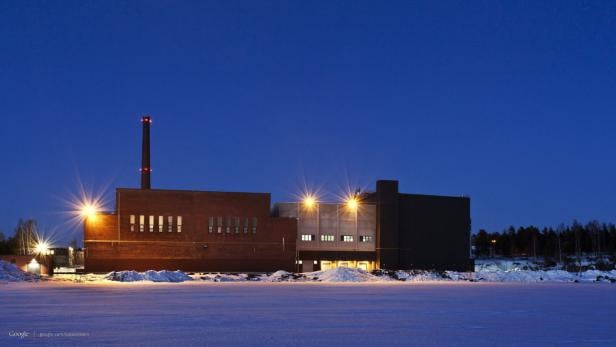 Ein Industriegebäude mit Schornstein steht im Winter unter blauem Himmel.