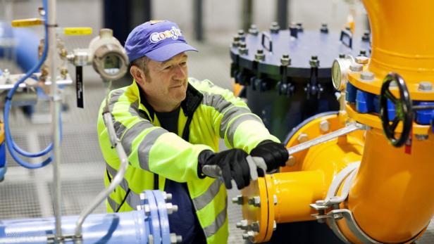 Ein Mann mit einer Google-Kappe arbeitet an einem gelben Rohr mit einer Rohrzange.