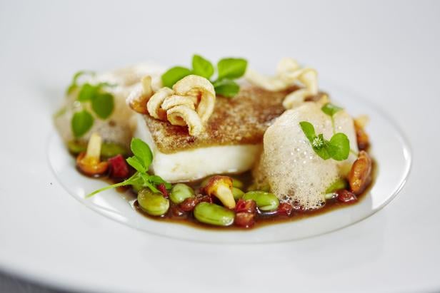 Ein Teller mit einem Stück Fisch, Bohnen, Pilzen und einer hellen Soße.