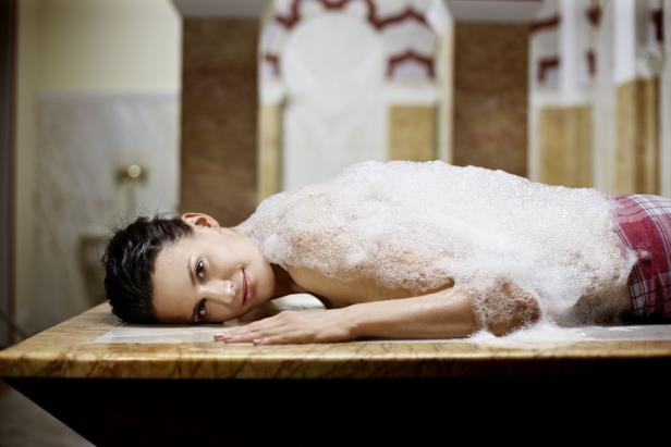 Eine Frau liegt mit Schaum bedeckt auf einem Marmortisch.