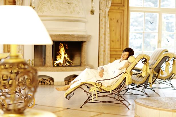Eine Frau entspannt in einem Bademantel vor einem Kamin in einem luxuriösen Ambiente.