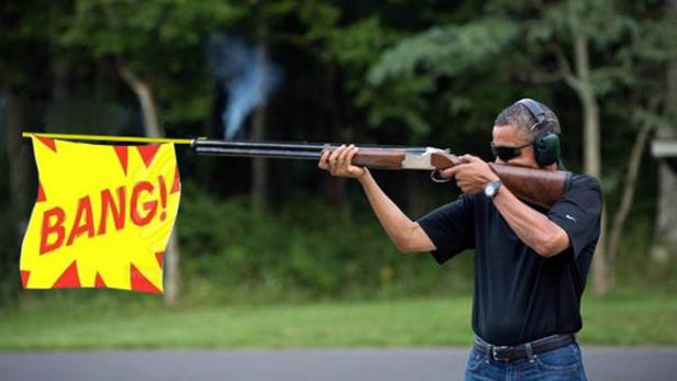 Ein Mann mit Kopfhörern und Sonnenbrille schießt mit einem Gewehr, an dem ein gelbes „BANG!“-Schild befestigt ist.