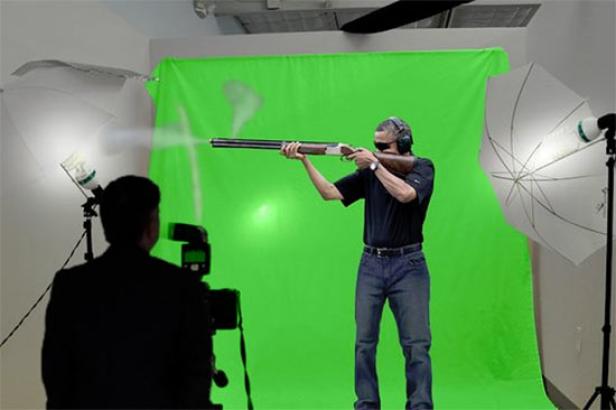 Ein Mann schießt mit einem Gewehr vor einem Greenscreen, während er von einem Fotografen aufgenommen wird.