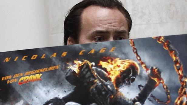 Nicolas Cage hält ein Poster des Films „Ghost Rider: Spirit of Vengeance“ vor sein Gesicht.