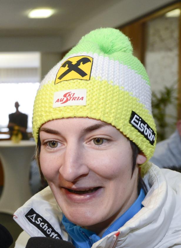 Eine Frau mit einer gelb-weiß-grünen Mütze von Ski Austria lächelt.