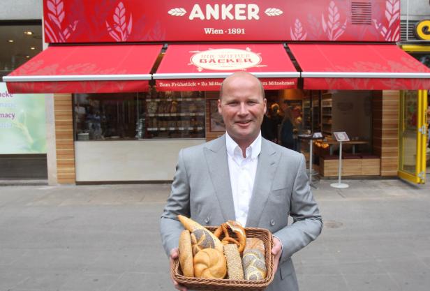 Ein Mann hält einen Korb mit Backwaren vor einer Filiale der Bäckerei Anker.