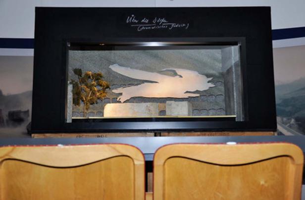 Ein Diorama mit einer stilisierten Darstellung eines Vogels und einem Baum hinter Glas.
