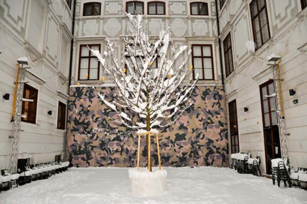 Ein schneebedeckter Baum steht in einem Innenhof mit einem Tarnmuster an der Wand.