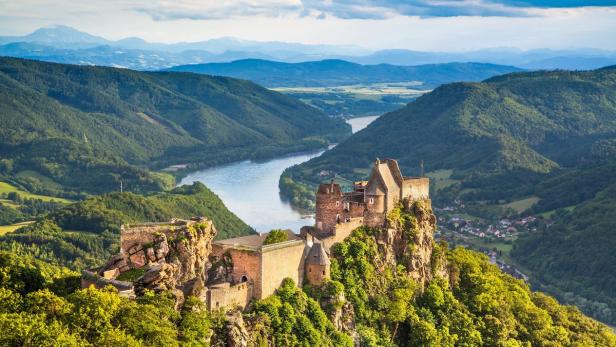 Die Burgruine Aggstein thront über der Donau, umgeben von bewaldeten Hügeln.