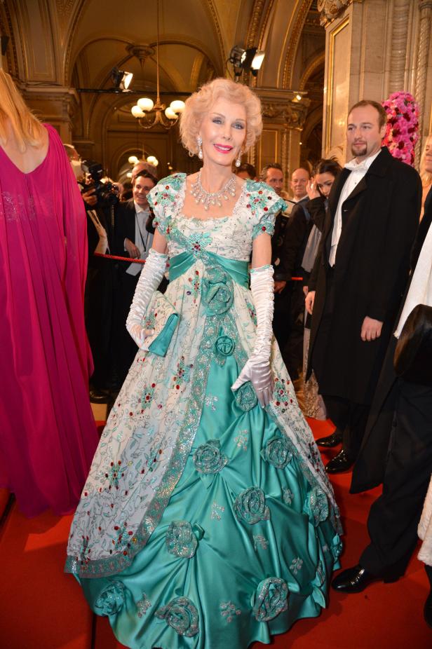 Eine ältere Frau in einem aufwendigen, türkisfarbenen Ballkleid auf dem roten Teppich.