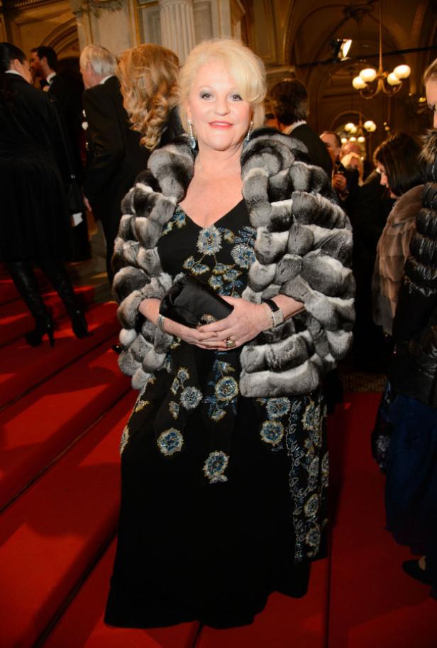 Eine Frau in einem Abendkleid und einem Pelzmantel auf einem roten Teppich.