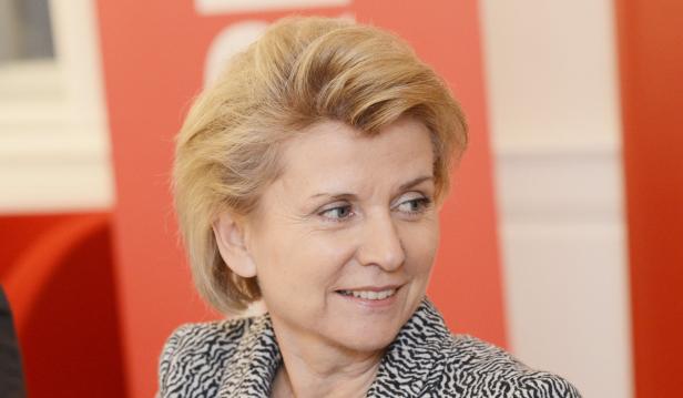 Eine Frau mit blonden Haaren lächelt und schaut zur Seite.