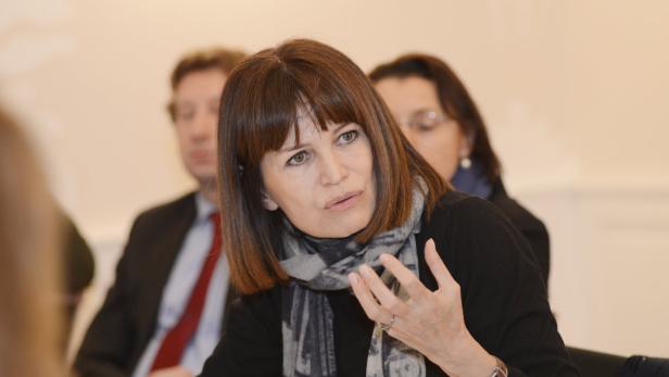 Eine Frau mit einem Schal gestikuliert während einer Besprechung.