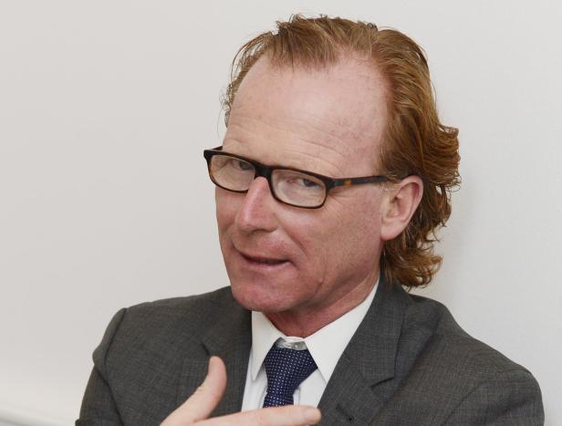 Ein Mann mit rötlichen Haaren, Brille und Anzug gestikuliert.