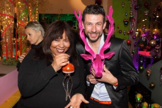 Zwei Personen posieren mit einer pinkfarbenen Rentier-Kopfbedeckung und einer verzierten Weihnachtskugel.