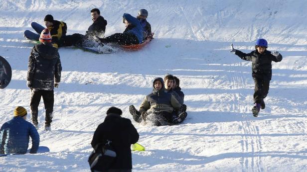 Eine Gruppe von Menschen rodeln einen schneebedeckten Hügel hinunter.