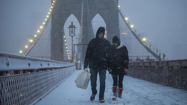 Ein Paar geht bei Schneefall auf der Brooklyn Bridge entlang.